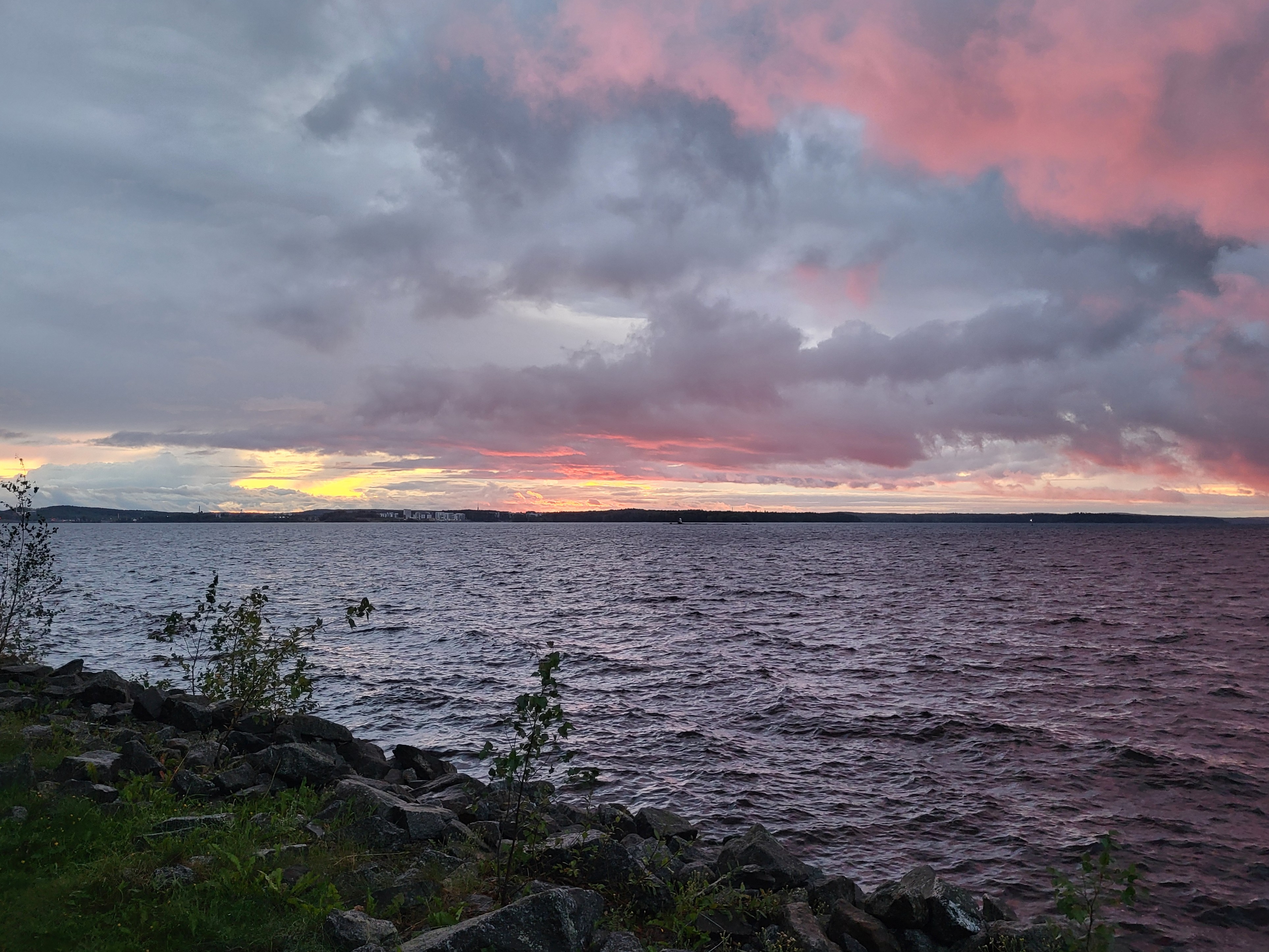 Spiegelstil Fins meer bij zonsondergang met roze wolken en een bootje in de verte