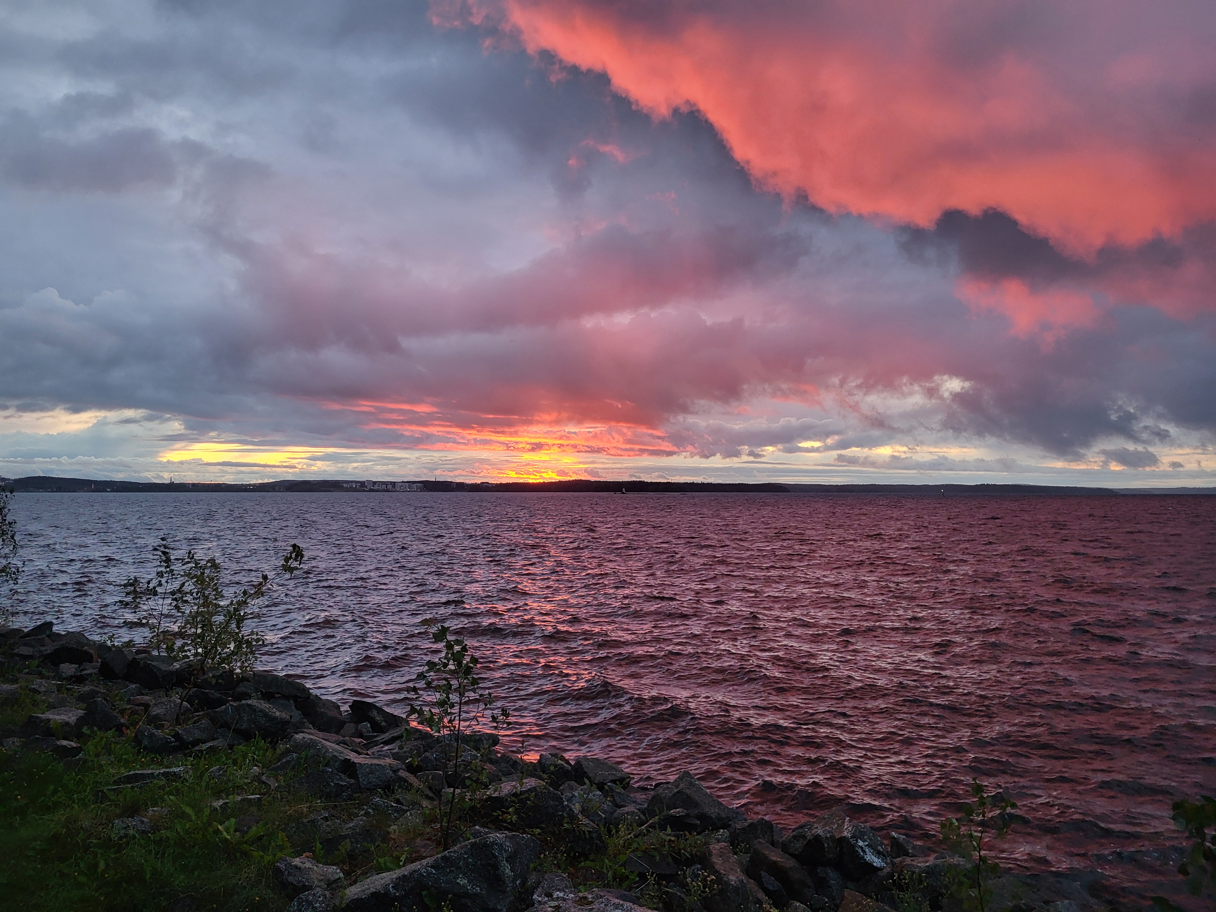 Donkere bewolkte avond met een geel glinsteren aan de horizon boven een ruige Finse oever